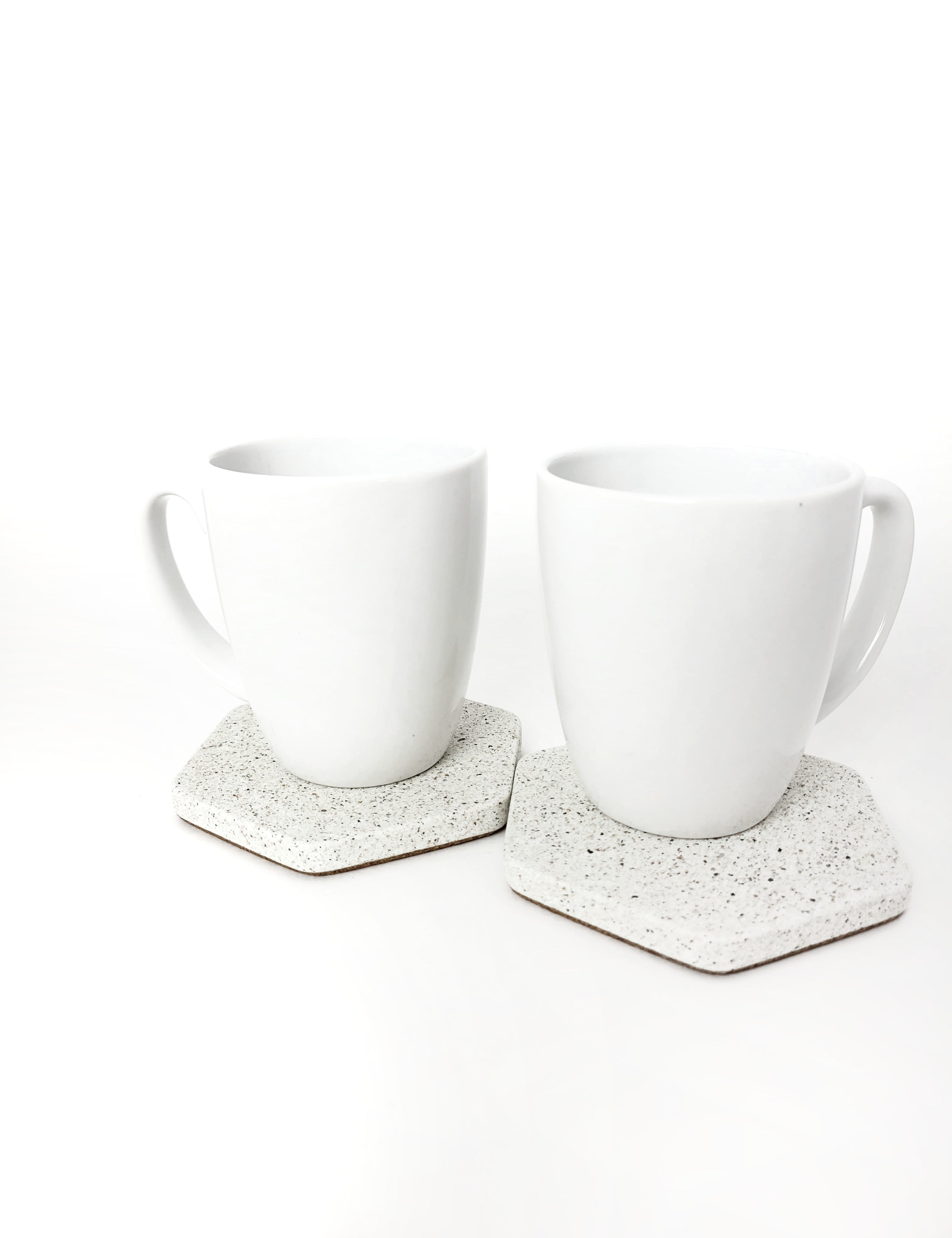Two white sandstone hexagon coasters side by side, one with a white coffee cup resting on top of one.