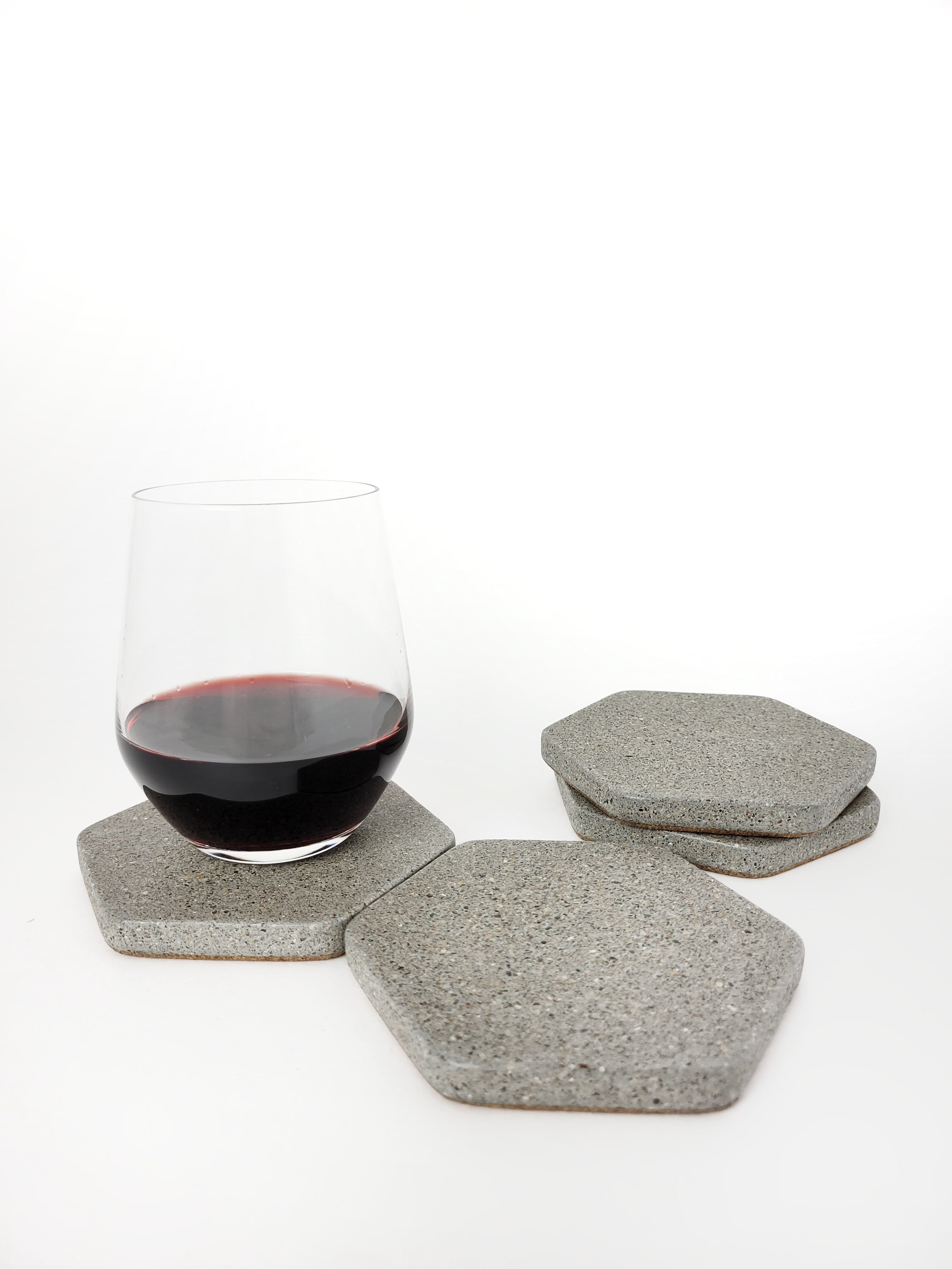Four grey sandstone concrete hexagon coasters displayed with a glass of red wine.