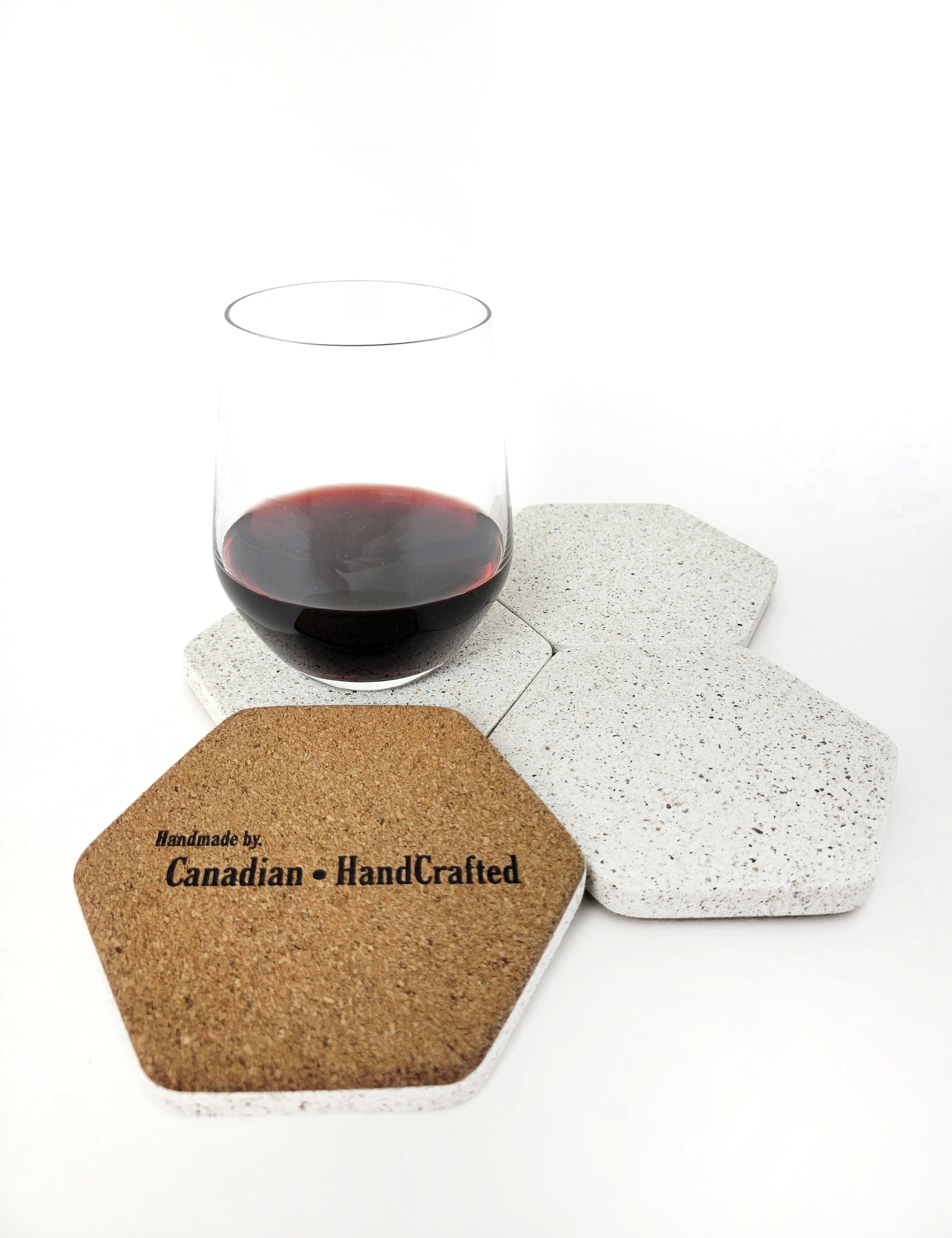 Four white sandstone concrete hexagon coasters displayed with a glass of red wine, one of the coasters is flipped upside-down displaying a soft cork bottom.