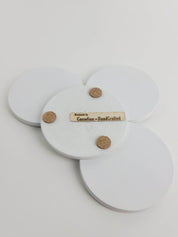 Set of 4 chalk white concrete coasters, one flipped to reveal the underside featuring 3 cork bumpers and an engraved wooden veneer with the text 'Handmade by Canadian HandCrafted'.