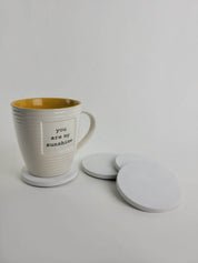 Set of 4 chalk white concrete coasters with a coffee mug resting on one, showcasing elegant home decor.