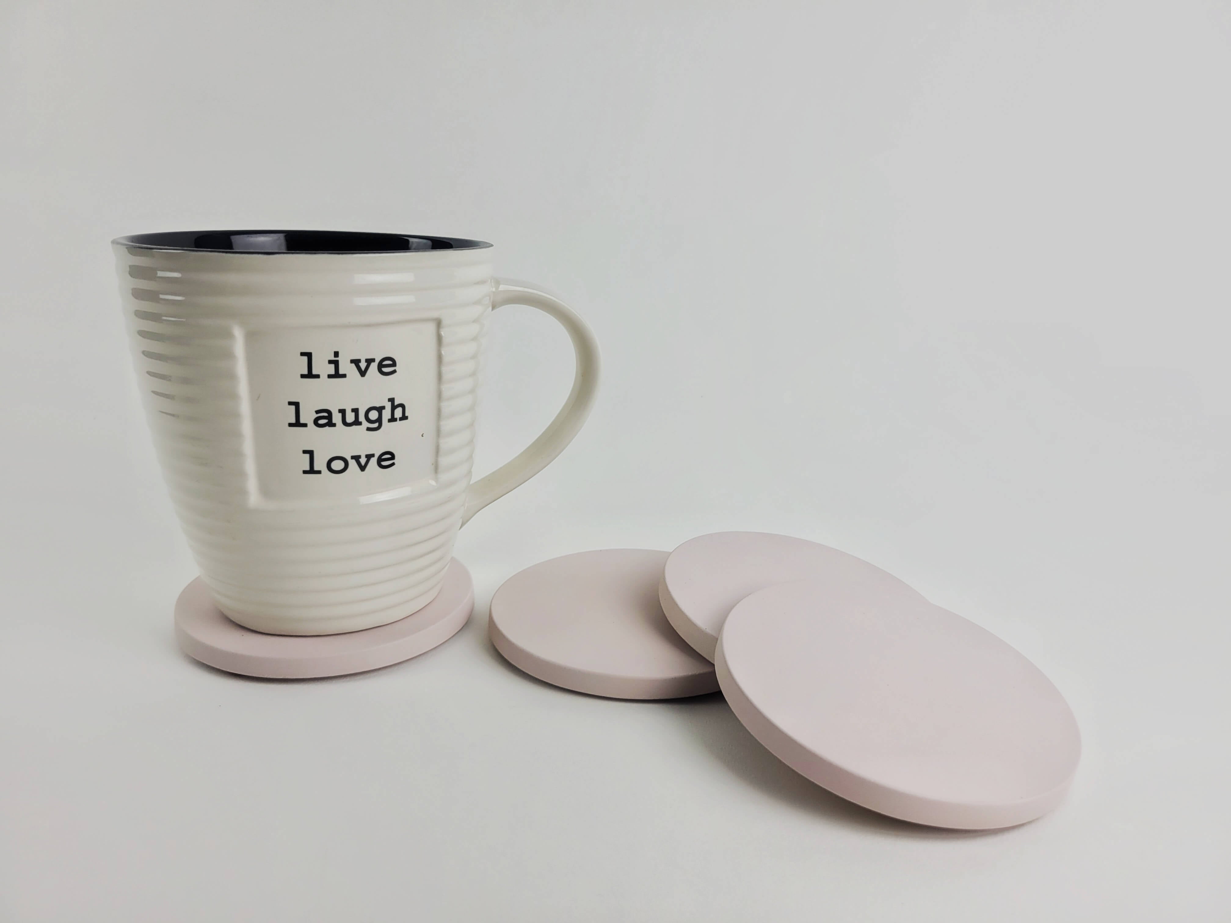 Set of 4 pastel pink concrete coasters with a coffee mug resting on one, showcasing elegant home decor.