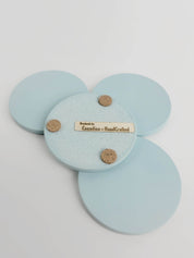 Set of 4 pastel turquoise concrete coasters, one flipped to reveal the underside featuring 3 cork bumpers and an engraved wooden veneer with the text 'Handmade by Canadian HandCrafted'.