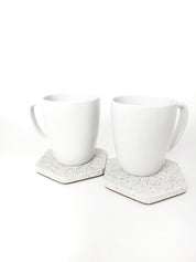Two white sandstone hexagon coasters side by side, one with a white coffee cup resting on top of one.