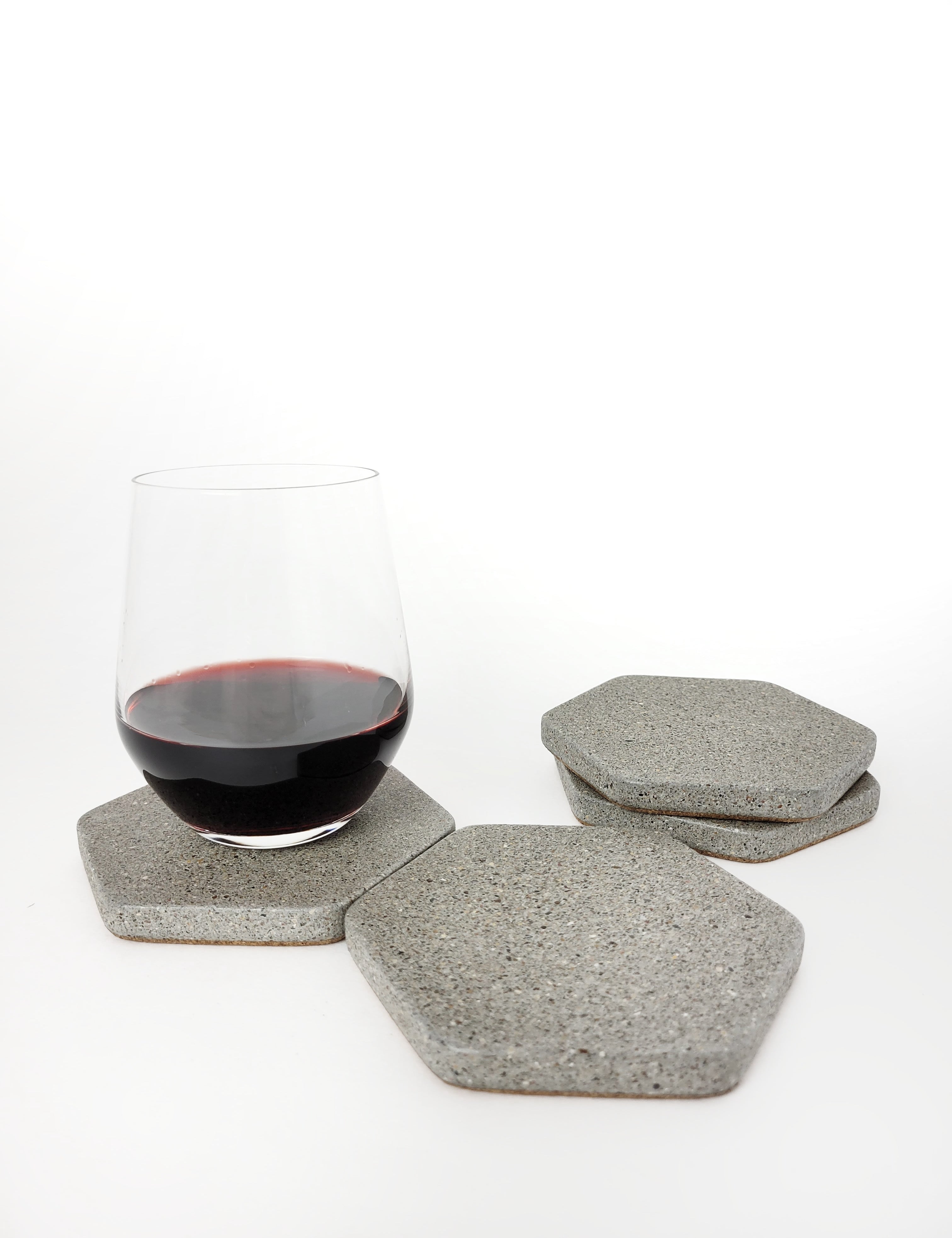 Four grey sandstone concrete hexagon coasters displayed with a glass of red wine.