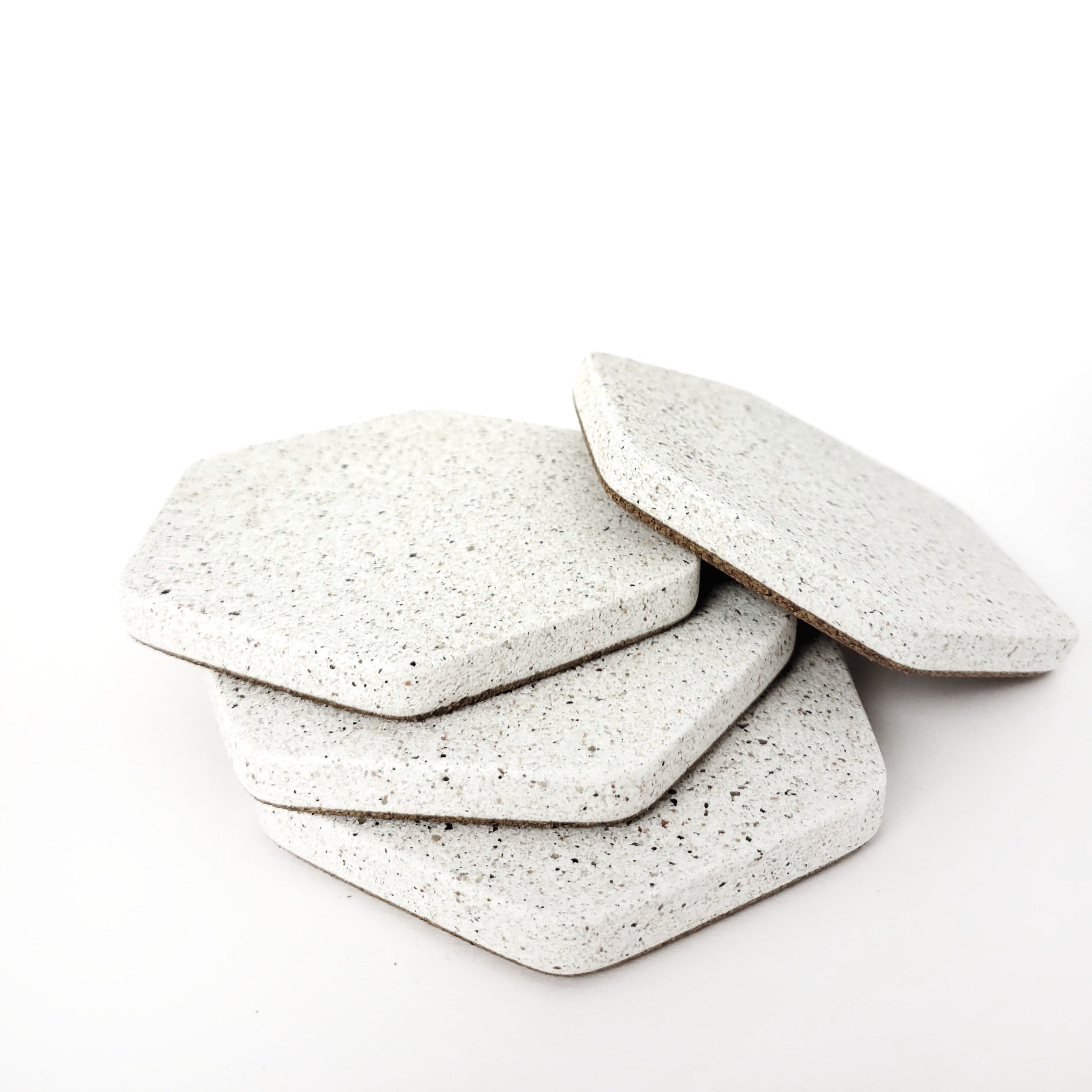 Four white sandstone concrete hexagon coasters displayed loosely stacked on top of eachother.