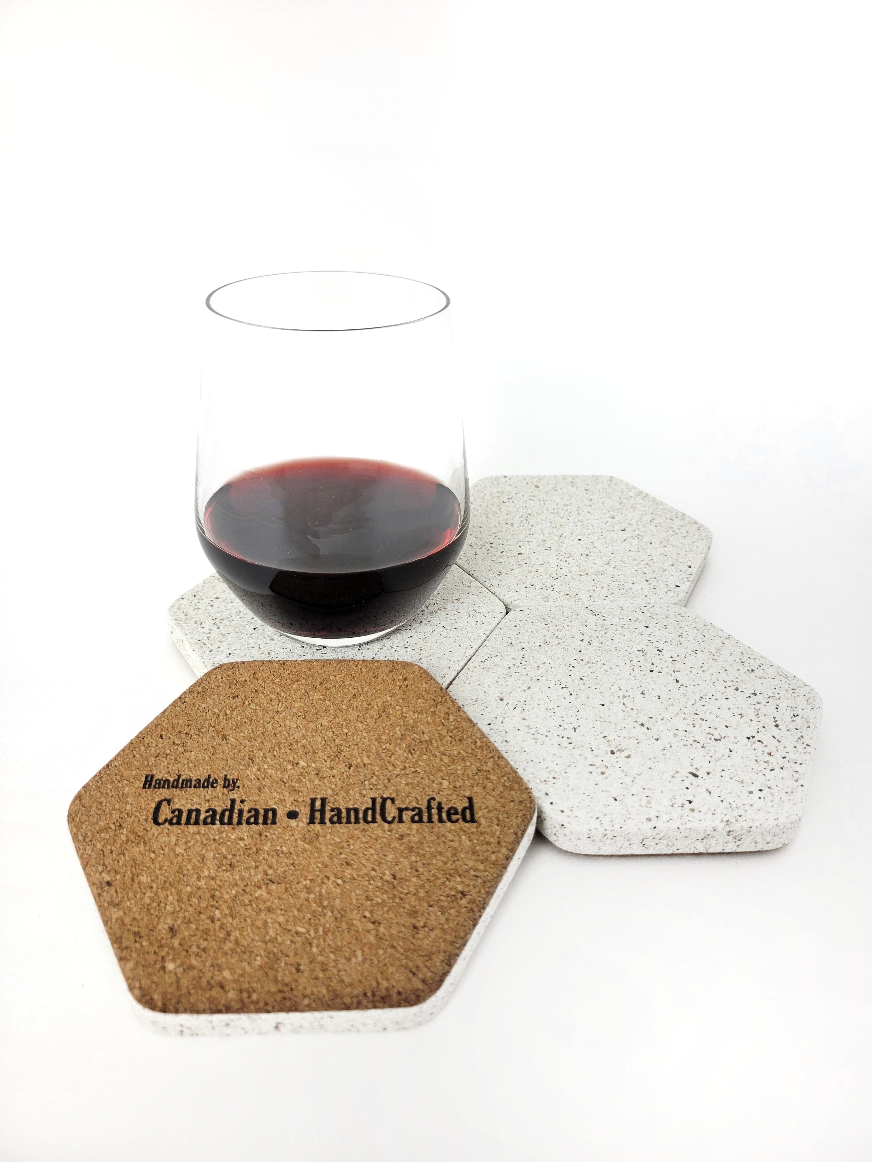 Four white sandstone concrete hexagon coasters displayed with a glass of red wine, one of the coasters is flipped upside-down displaying a soft cork bottom.