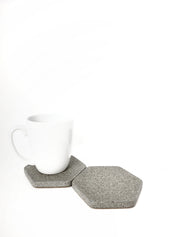 Two grey sandstone hexagon coasters side by side, one with a white coffee cup resting on top of one.