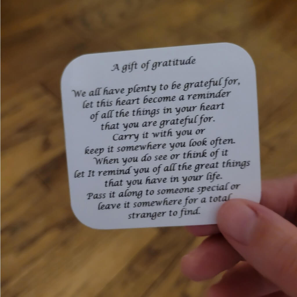 A gift of gratitude note with rounded corners being help by a hand reading, "We all have plenty to be grateful for. Let this heart become a reminder of all the things in your hearts that you are grateful for. Carry it with you or keep it somewhere you look often. When you do see or think of it let it remind you of all the great things that you have in your life. Pass it along to someone special or leave it somewhere for a total stranger to find."