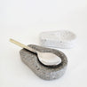 A grey and white terrazzo stone spoon rest. A gold and silver spoon rests on the grey sandstone spoon holder.