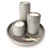 Three grey terrazzo stone tealight holders lit sitting on a grey terrazzo round stone tray.
