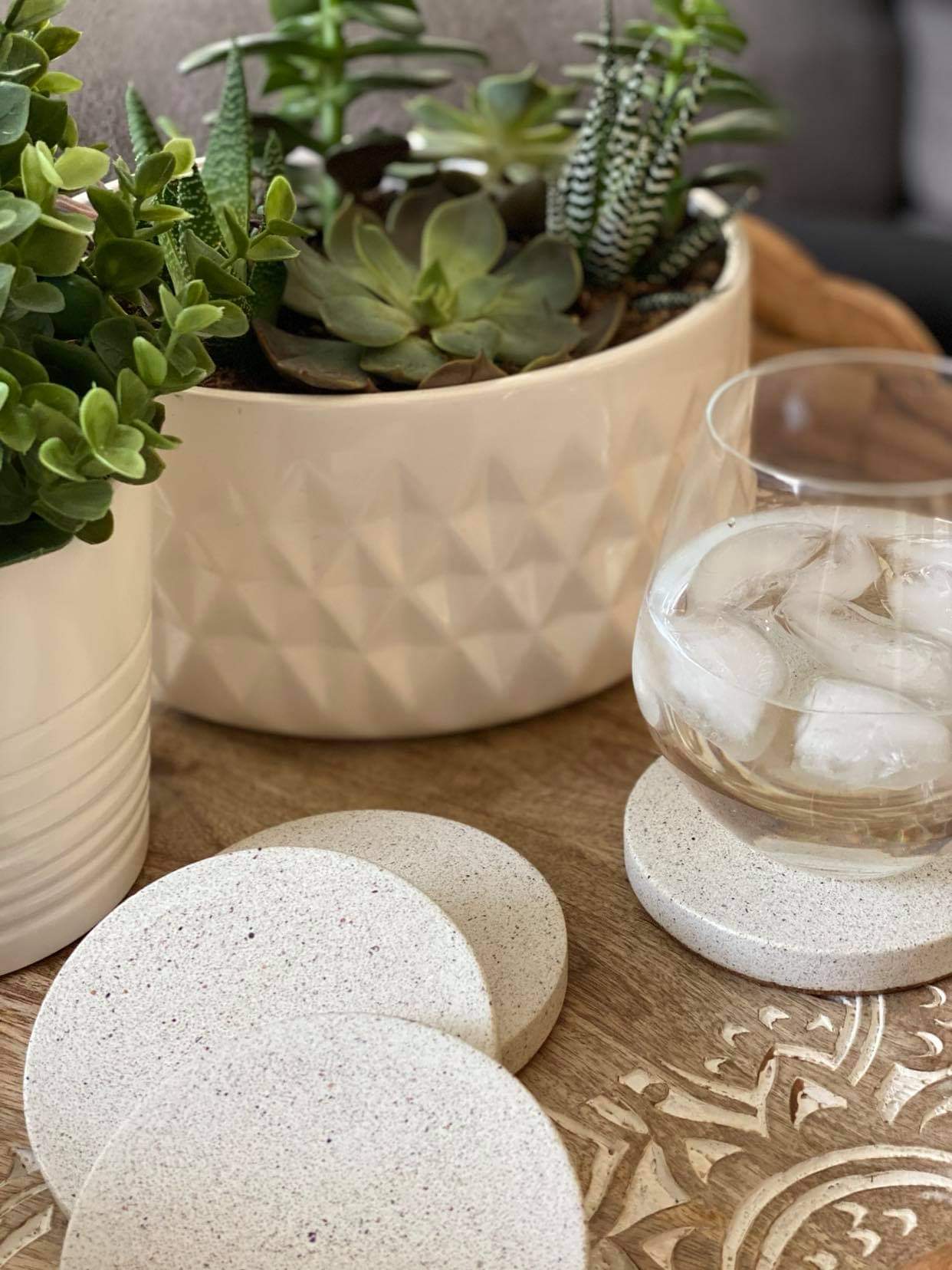 Set of 4 sparkling white concrete stone coasters, featuring one with a glass of water and ice, complemented by two green plants in minimalist white porcelain planters.